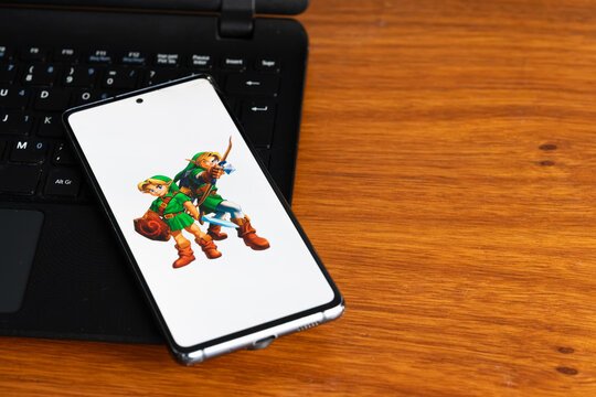Punta Arenas, Chile &ndash; July 3, 2026: A close-up of a mobile phone showcasing characters from The Legend of Zelda: Ocarina of Time gaming franchise, placed on top of a black laptop on a wooden desk