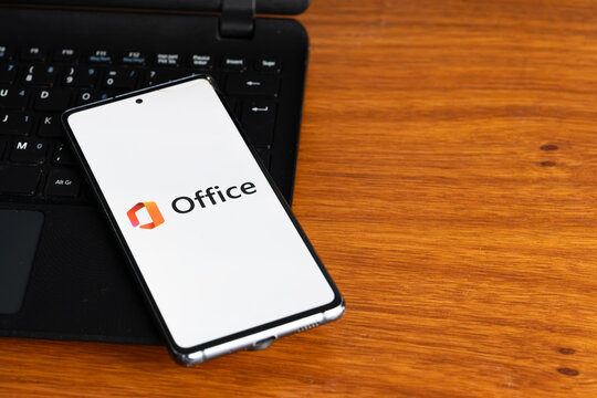 Punta Arenas, Chile &ndash; July 3, 2026: The Microsoft Office logo displayed on a smartphone screen resting on a laptop keyboard over a wooden table background
