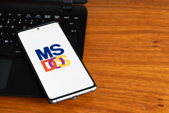 Punta Arenas, Chile &ndash; July 3, 2026: The classic MS-DOS operating system logo displayed on a smartphone screen resting on a laptop keyboard over a wooden table background