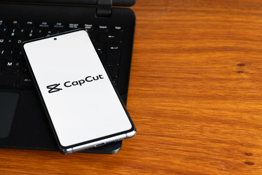 Punta Arenas, Chile &ndash; July 8, 2026: The CapCut video editing application logo displayed on a smartphone screen resting on a laptop keyboard over a wooden table background