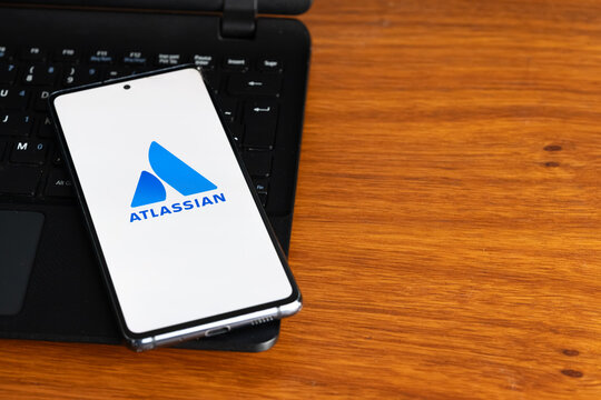 Punta Arenas, Chile &ndash; July 8, 2026: The Atlassian software company logo displayed on a smartphone screen resting on a laptop keyboard over a wooden table background