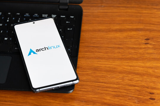 Punta Arenas, Chile &ndash; July 8, 2026: The Arch Linux operating system logo displayed on a smartphone screen resting on a laptop keyboard over a wooden table background