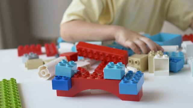Close-up of child constructing bridge from colorful plastic blocks. Creative educational game promotes imagination, logical thinking, engineering concepts, coordination and fine motor development.