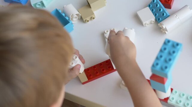 Top view of child arranging colorful construction pieces on white table. Educational creative activity develops imagination, planning, spatial awareness, fine motor coordination and logical thinking.