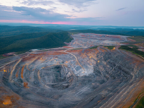 Aerial view of expansive open pit mine at dusk with surrounding landscape. Industry mining gold ore or nickel, zinc