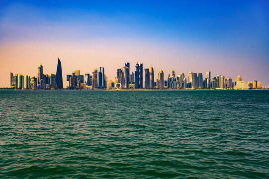 Modern skyscrapers of West Bay financial district in Doha at sunset seen across Doha Bay from the Corniche promenade with colorful gradient sky, Qatar