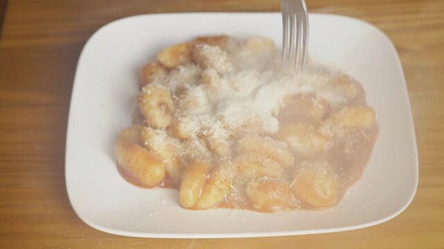 Close up of a fork picking up hot steaming potato gnocchi pasta with parmesan cheese, Person using a fork to eat delicious Italian gnocchi with red tomato sauce