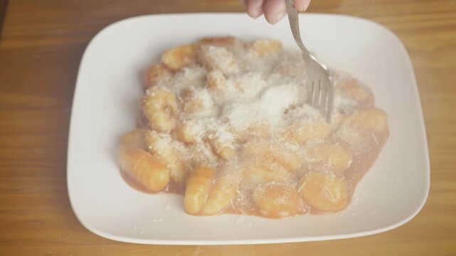 Close up of a fork picking up steaming potato gnocchi with parmesan cheese, Person eating delicious hot Italian gnocchi pasta with tomato sauce from a plate