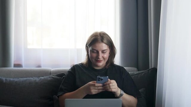 A person is smiling and looking at a phone in a relaxed indoor setting near a window with curtains. The scene conveys a lifestyle and technology theme, with the subject appearing happy.
