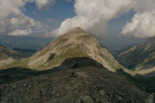 Aerial view of Pizzo Cefalone with rocky ridges, green mountain slopes, and a group of hikers resting on the summit in L'Aquila, Abruzzo, Italy.