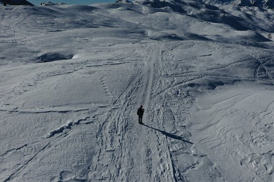Aerial view of a lone hiker standing on a vast snow-covered mountain slope in the Dolomites with deep shadows and textured snow patterns in Madonna di Campiglio, Trentino-Alto Adige, Italy.