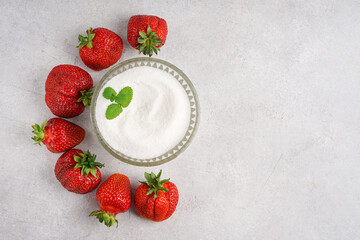 Top view of sugar bowl surrounded by fresh ripe strawberries with mint leaf. Concrete background with copy space. Healthy summer recipe flat lay. © Taborisova