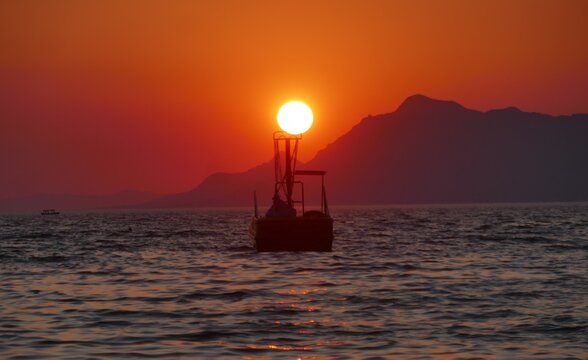 Fishing boat on the sea in magnificent colorful sunset with mountain and rays of sun scenic romantic sunset scenery