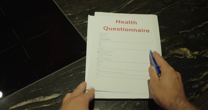 Close-up of a person reviewing a health questionnaire and pointing at the document with a blue pen. Concept of medical forms, healthcare documentation, patient information, and insurance applications.