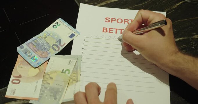 Close-up of a person writing sports betting notes on paper with cash placed beside it. Concept of gambling, betting strategy, financial risk, and sports wagering.