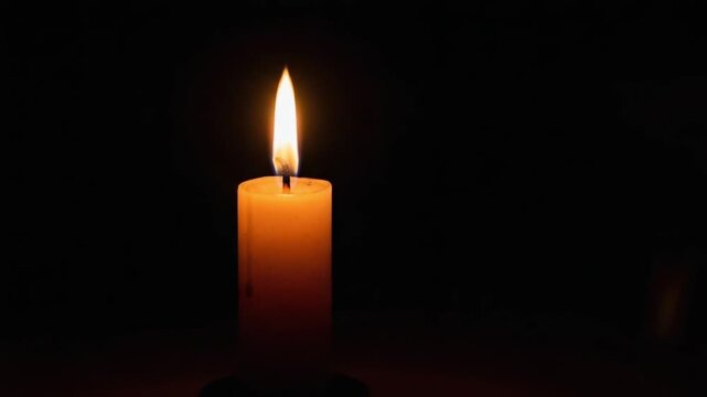 A single lit candle glowing in the dark against a black background