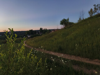 Obraz premium Green grass and blue sky in the wild in mountains road with meadow in evening sunset 