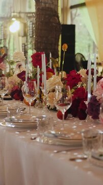 Vertical video. Wedding table setting with colorful flowers, candles and tableware under event tent.