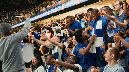 Fototapeta premium Fan leader with megaphone and drum energizing soccer supporters in stadium stands, family cheering and enjoying fun times with their son at stadium.