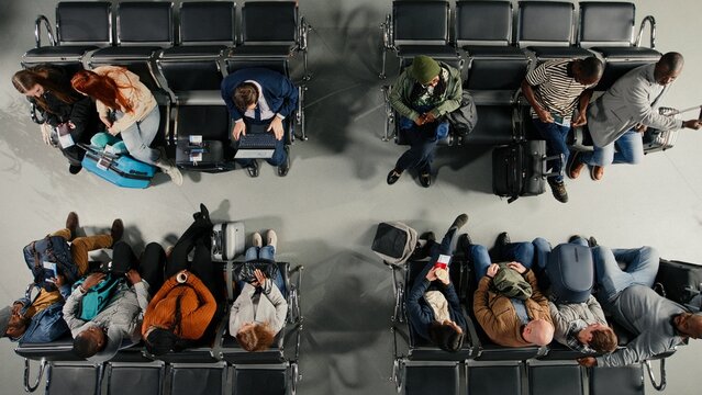Walking, top down view and crowd in busy airport sitting on chairs, Waiting on benches, high angle shot and passengers navigating chaotic transit hub environment before departure during flight.