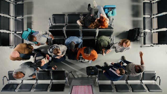 Top down view of troubled tourists in airport distressed by plane delays shown on departure board, Passengers upset by canceled flights announcement on FIDS.