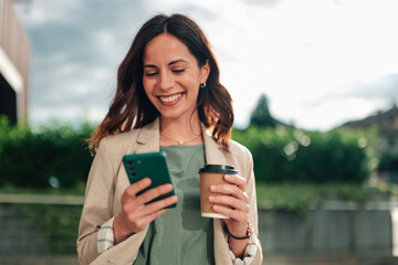 Smiling businesswoman checking smartphone on a coffee break outdoors, enjoying communication and casual business lifestyle
