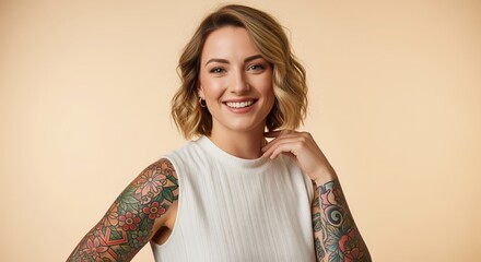 Obraz premium A young blonde woman with colorful tattoos on both arms smiles confidently at the camera. She wears a white ribbed sleeveless top against a beige background.
