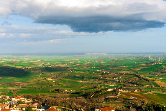 beautiful sunrise or sunset view from antique mediterranean town in Italy with vintage building roofs to a panoramiv green valley with green fields and hills and bright cloudy sky above horizon