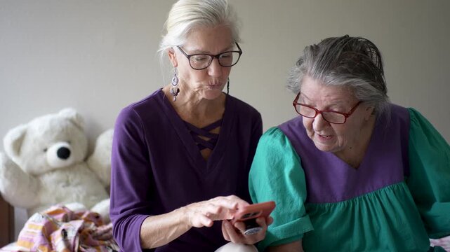 Mature daughter visits her elderly mother at the senior care facility. They talk, share photos, and enjoy their time together.