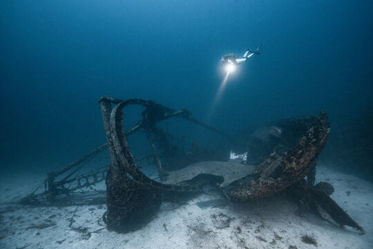 Vis, Split-Dalmatia County, Croatia - 27 June 2026: View of a scuba diver exploring a historic shipwreck on the sandy seabed, illuminated by a flashlight in the clear blue water.