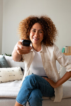 Woman smiling holding remote control watching television at home