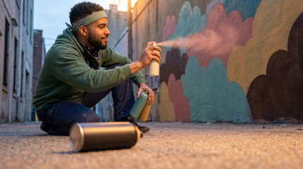 Fototapeta premium African American man painting graffiti art - Young man spray painting a colorful mural in urban alleyway 