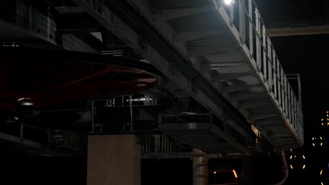 View of a cable car system at night showing the rail station, the cables, and the surrounding structures in a city setting