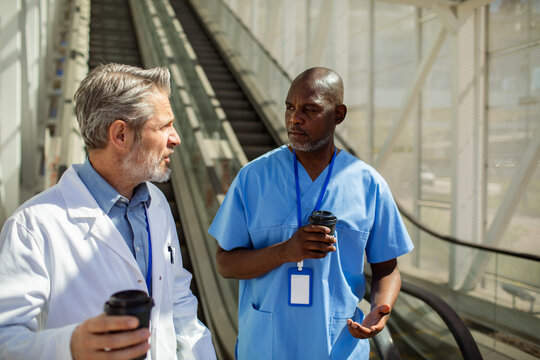 Two healthcare professionals talking with coffee in hospital corridor