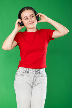 Passionate teenage girl in red T-shirt and jeans listening and dancing to music on headphones on a green background. Chroma key compositing