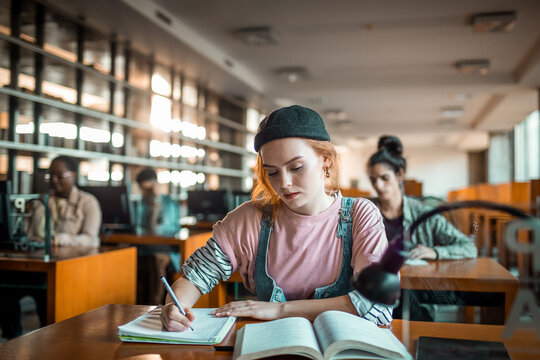 Focused college student writing notes in library