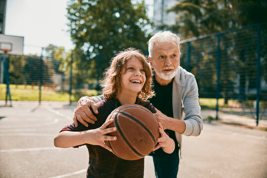 Grandfather coaching child playing basketball on outdoor court