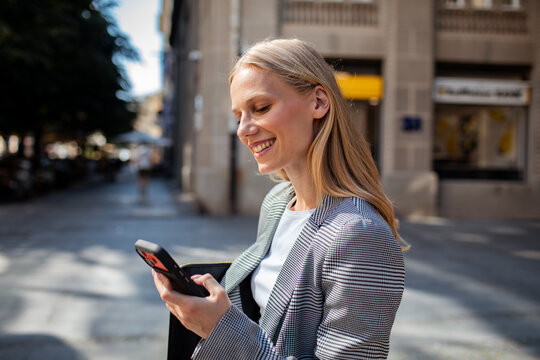 Smiling businesswoman using smartphone on city street
