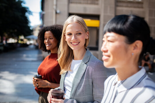 Smiling coworkers walking with coffee on a city street