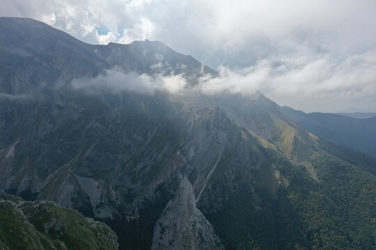 Aerial view of the rugged Corno Piccolo mountain peak with steep rocky slopes, patches of green vegetation, and scattered clouds in Pietracamela, Abruzzo, Italy.