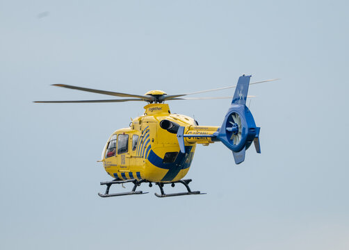 North West Air Ambulance helicopter in flight flying away from the camera in to a grey muggy sky fto the scene of a medical emergency .