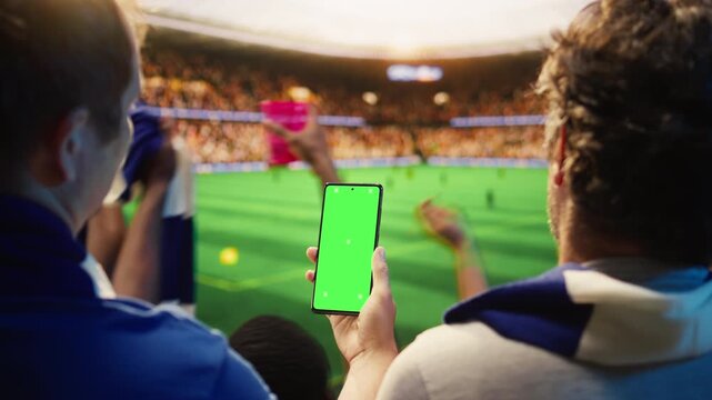 Close up of mockup phone used by fan in stadium to compare odds during soccer match day, showing football supporter checking predictions on live score app on green screen smartphone.