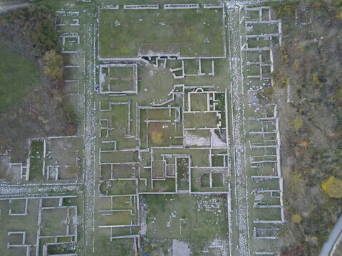 Aerial view of the ancient Roman archaeological site of Alba Fucens with stone foundations, walls, and pathways surrounded by trees in Albe, Abruzzo, Italy.