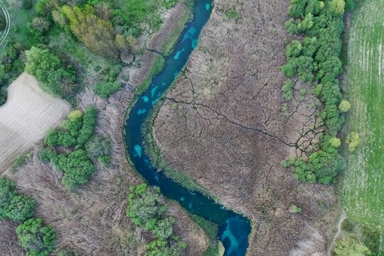 Aerial view of the Tirino River winding through lush vegetation and fields in Capestrano, Abruzzo, Italy.