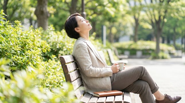 Asian woman relaxing on park bench with coffee cup, mindful break in nature, peaceful professional taking a moment of calm outdoors