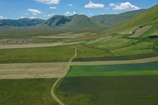 Aerial view of the vast plains of Castelluccio with colorful agricultural fields and rolling green hills in Castelluccio, Umbria, Italy.