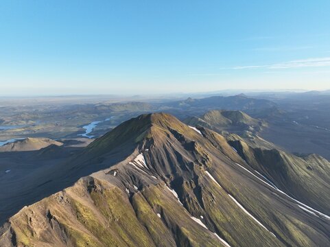 Aerial view of Langisjor mountain range with rugged volcanic slopes, patches of snow, and winding rivers in the distance in Kirkjubaejarklaustur, Skaftarhreppur, Iceland.
