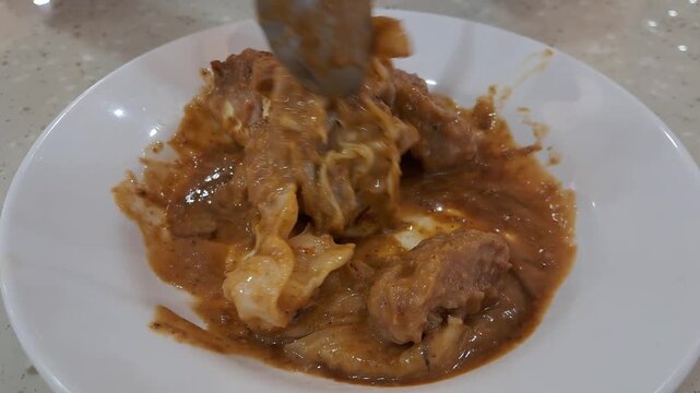 A close up shot of traditional Indonesian steamed fish dumplings or siomay being mixed and drenched with rich savory peanut sauce gravy.