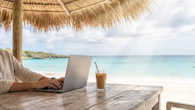Freelancer working on laptop with iced coffee at a tropical beach resort