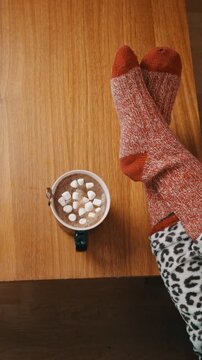High angle shot of cozy winter morning with hot cocoa mug and relaxed feet on wooden table